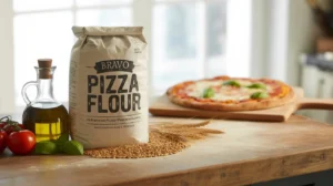Bravo Pizza Flour bag on a wooden counter with olive oil, tomatoes, wheat grains, and a fresh pizza in the background.