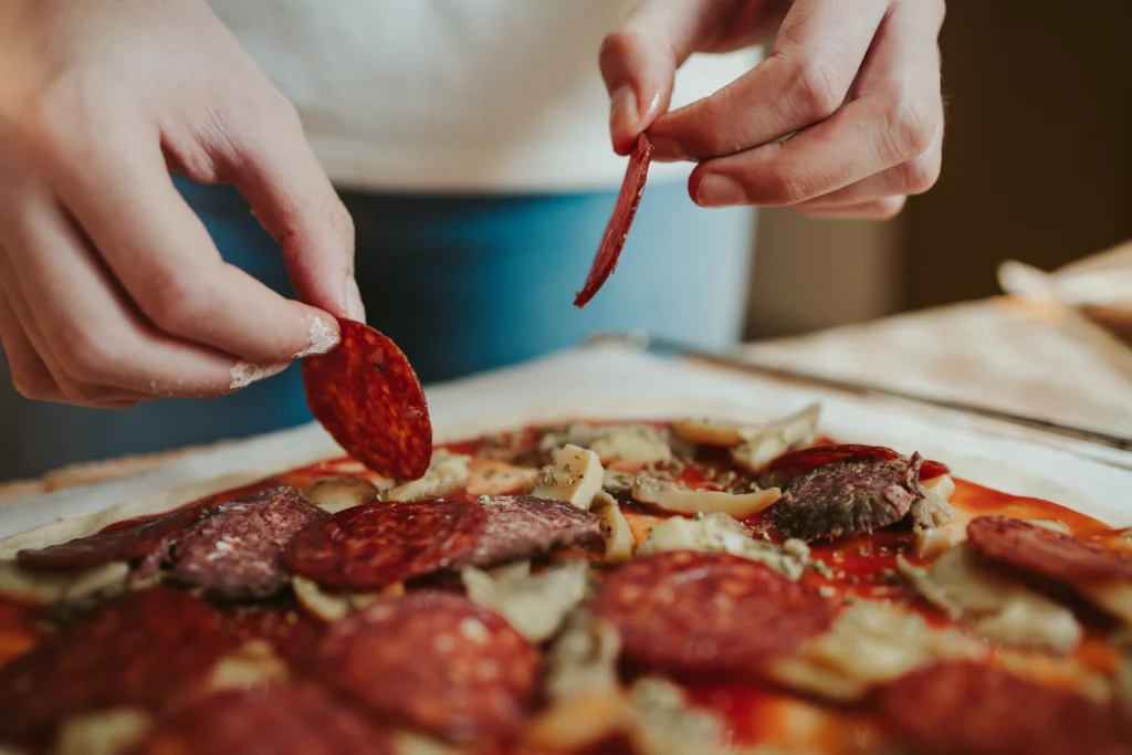 Chef preparing a Hawaiian pizza with pineapple and ham, showing creative pizza topping ideas for home and restaurant menus.