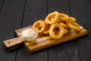 Golden crispy onion rings served on a wooden board with creamy dipping sauce, illustrating how to prepare onion rings at home.