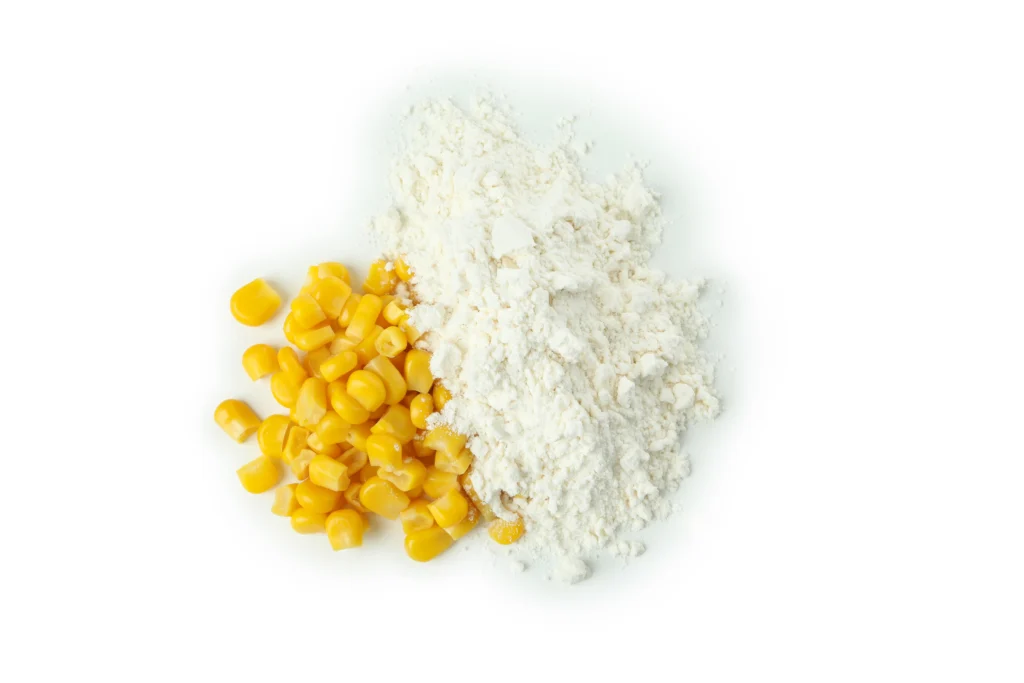 Pile of yellow corn kernels next to a mound of white corn flour on a white background.