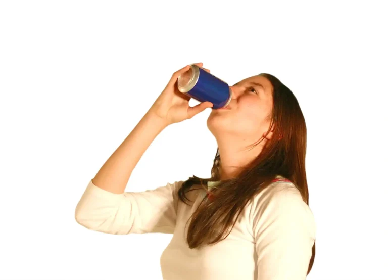 A young person tilting their head back while drinking from a blue beverage can against a white background.