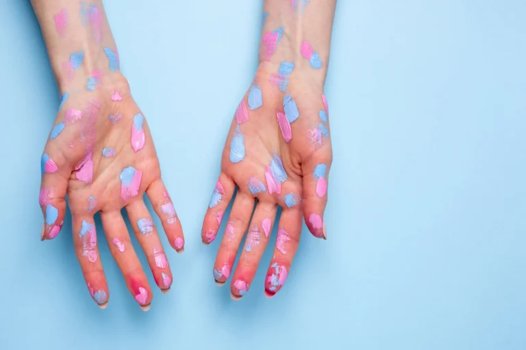 Two open hands covered in pink and blue watercolor paint against a light blue background.
